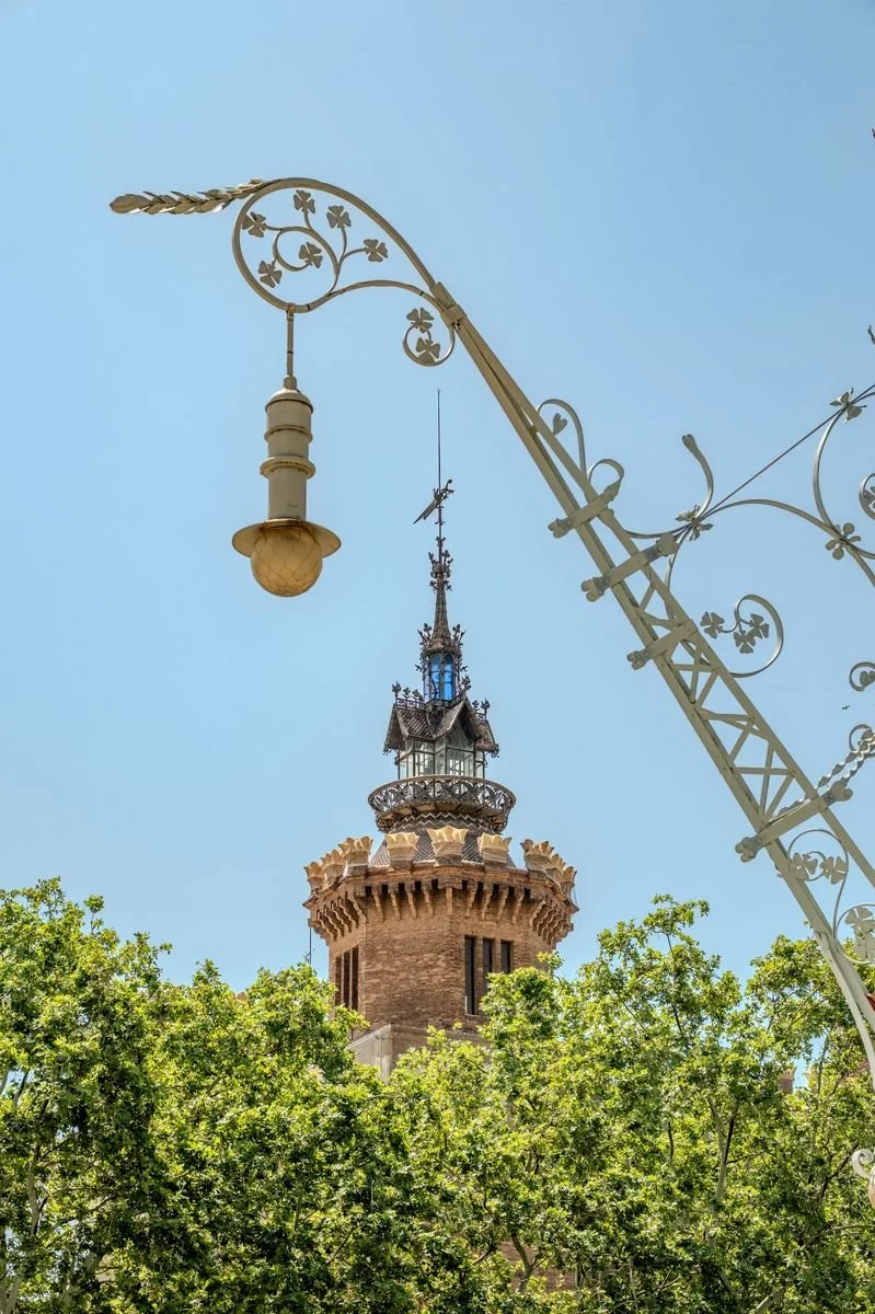 An ornate wrought-iron street lamp stands before the Castell dels Tres Dragons' turreted tower