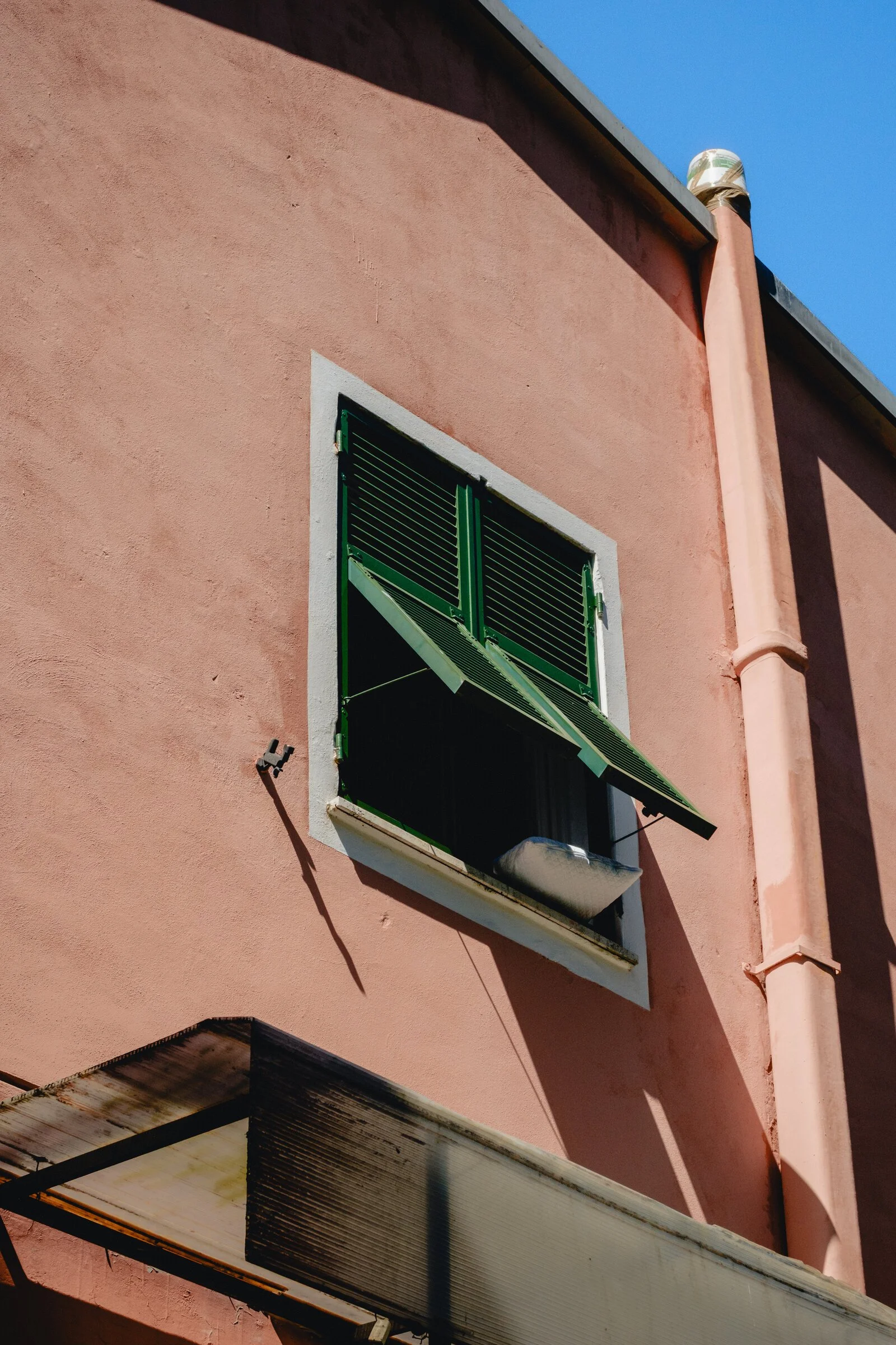 A green shutter thrown open against a bright watermelon-pink stucco wall