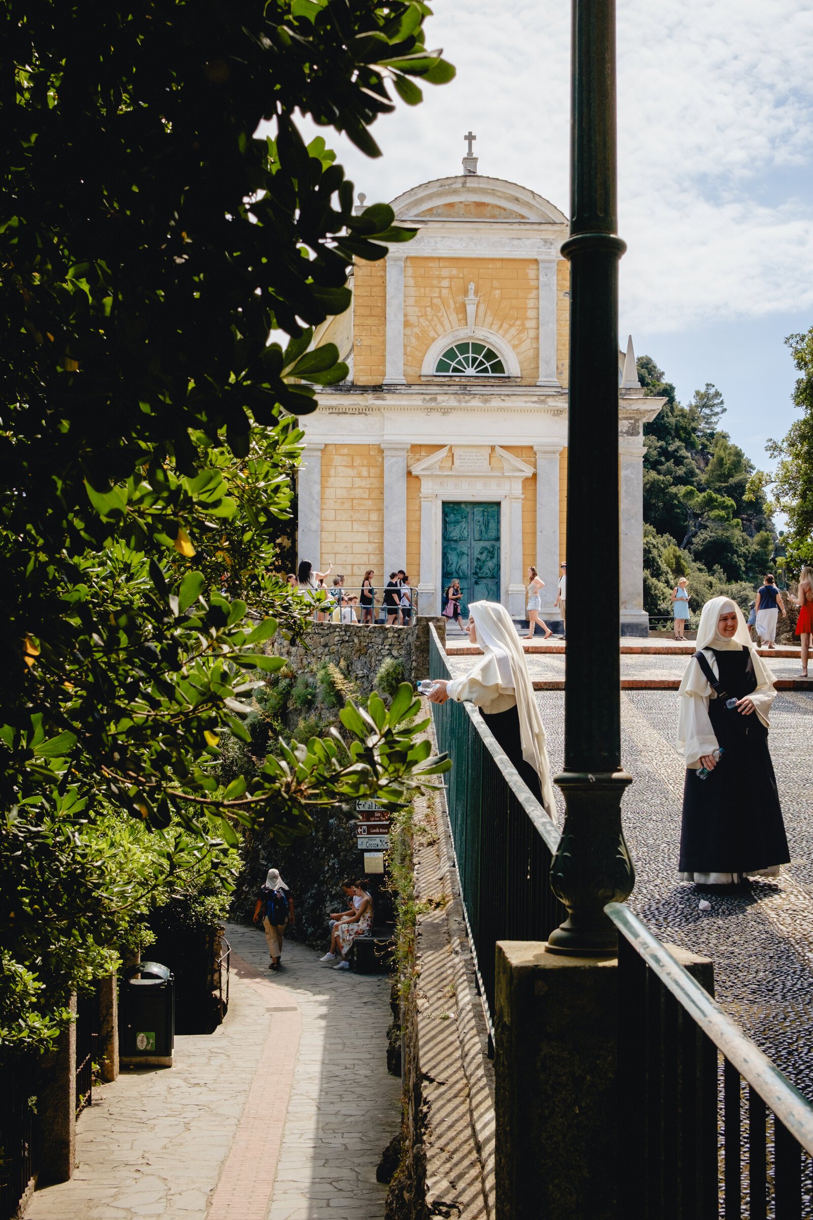 Two nuns pause on a promenade before Portofino's yellow baroque church, San Giorgio