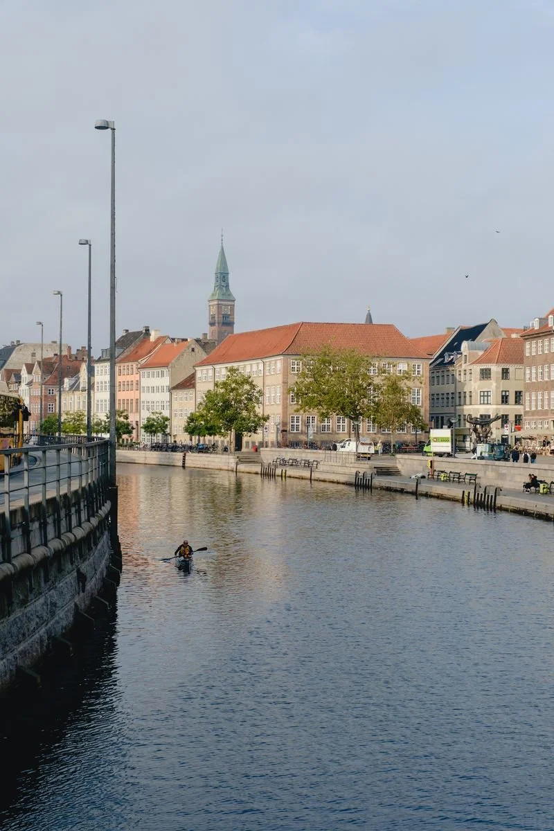 A kayaker paddles a Copenhagen canal past colorful buildings and a church spire