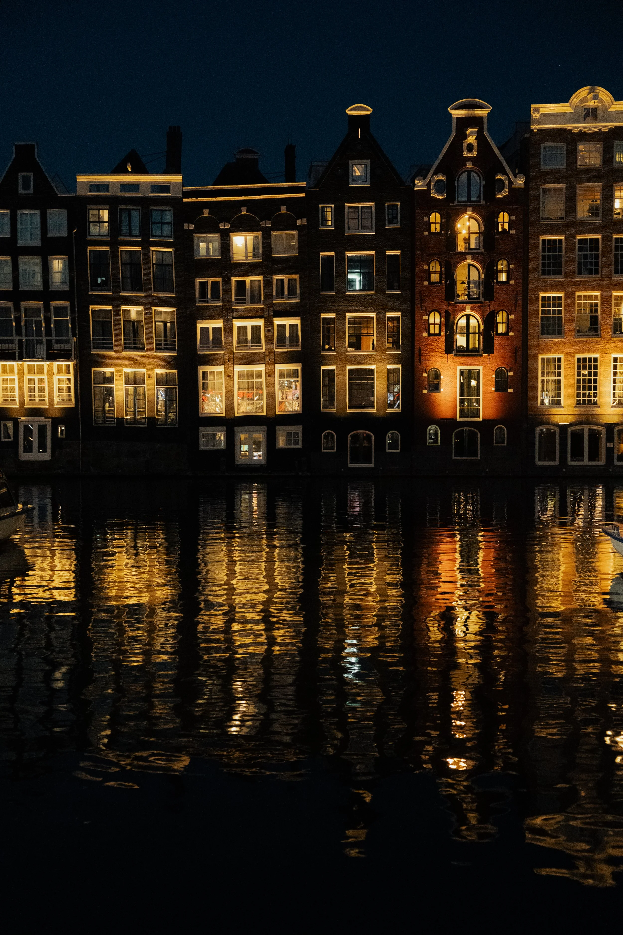 Nighttime view of historic buildings along a canal, with illuminated windows and reflections on the water.