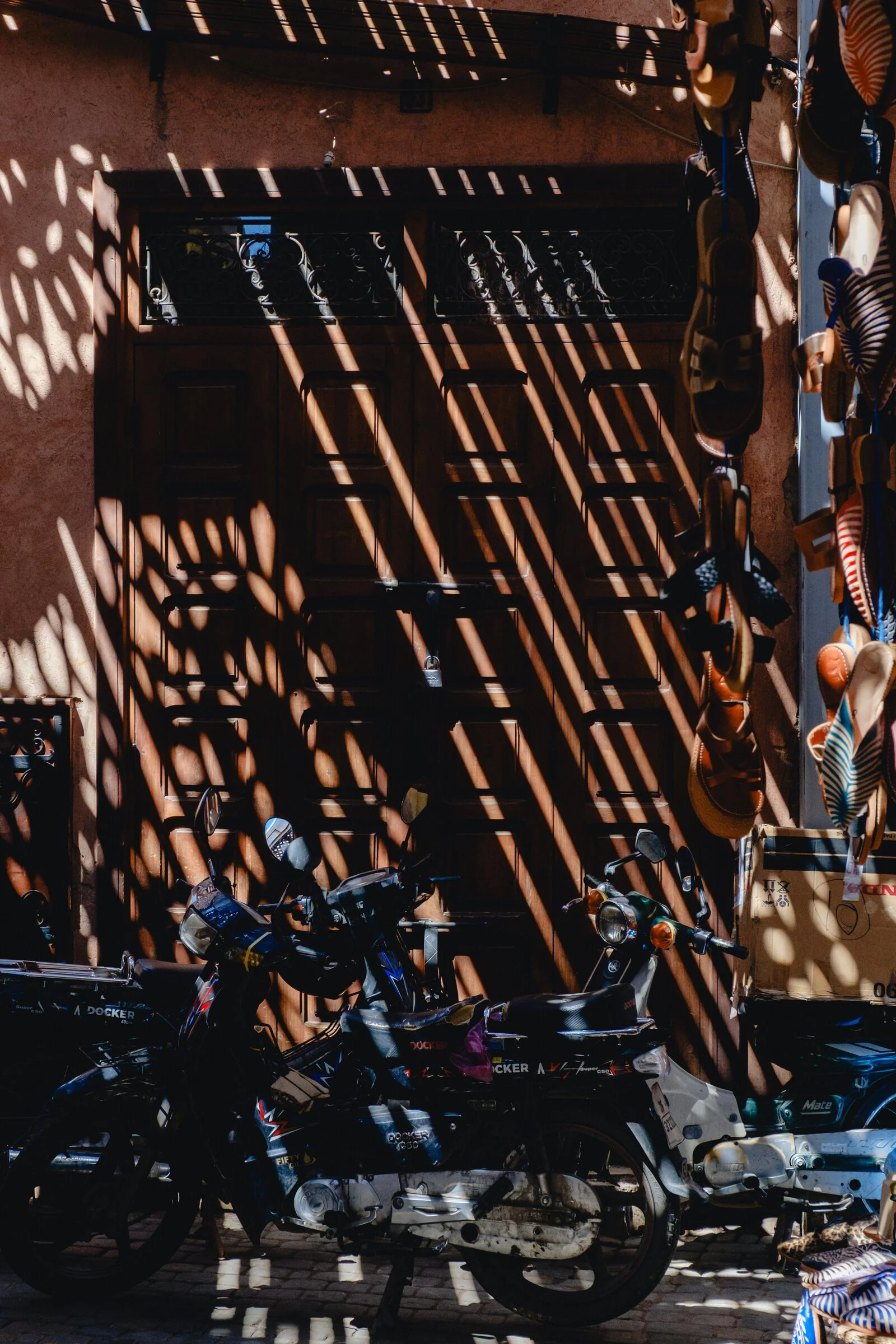 Dramatic diagonal shadows fall across a weathered wooden door and a parked motorbike