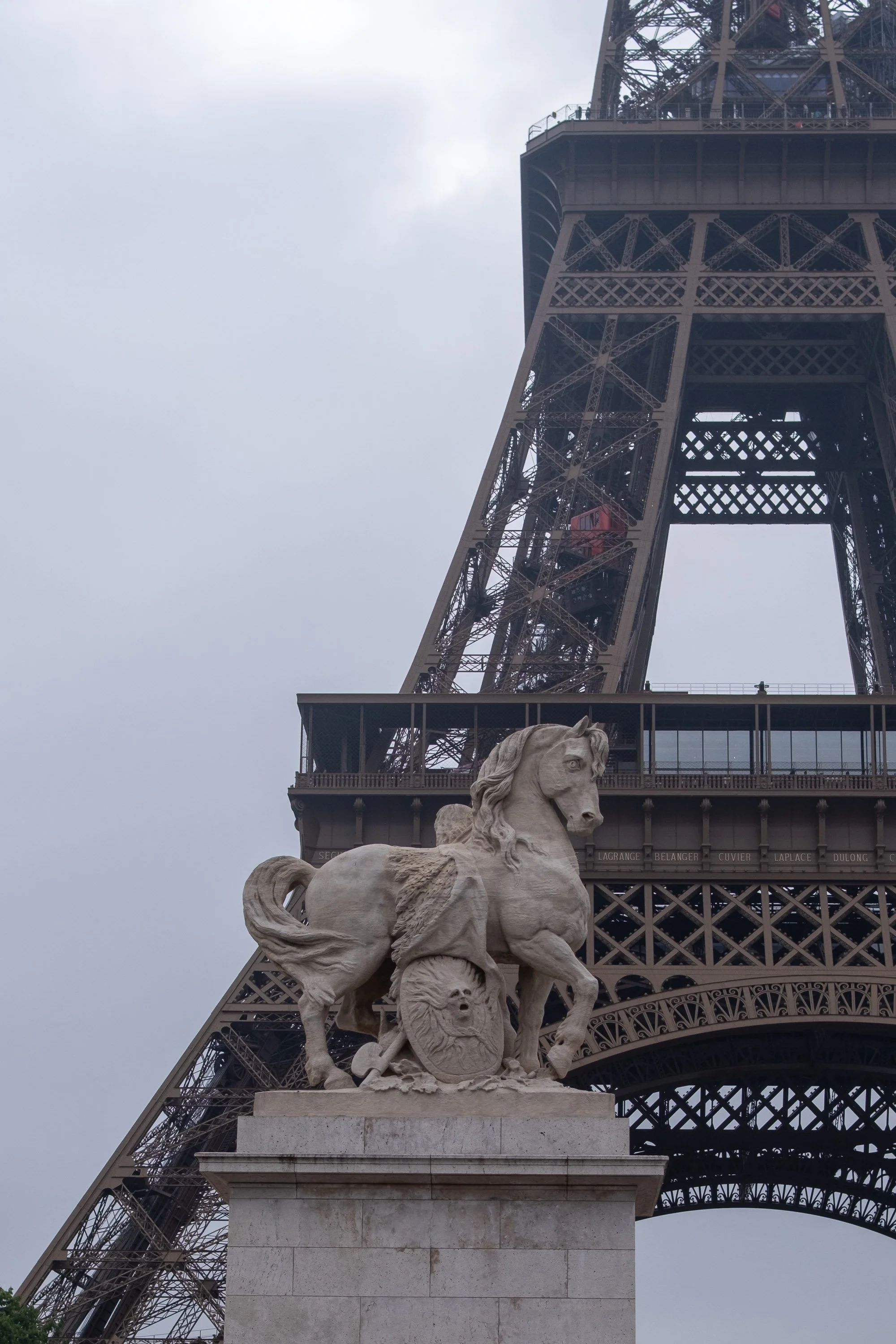 A stone statue of a horse with a shield and sword, positioned in front of the Eiffel Tower in Paris, France.