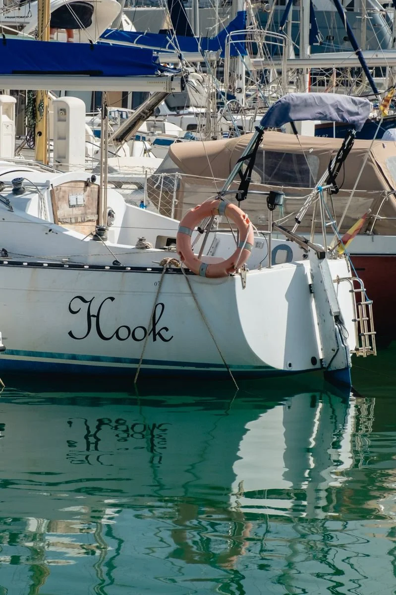 A sailboat named Hook reflects in the marina's still green water