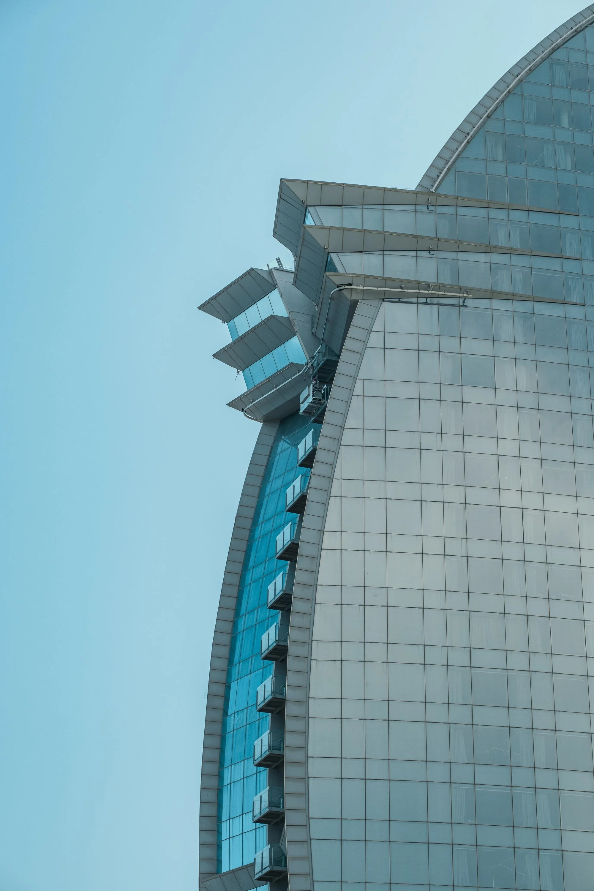 Close-up of the top part of a modern, glass-covered skyscraper with protruding balconies and an overcast sky in the background.
