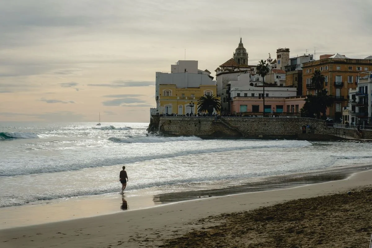 Sitges' seafront church and colorful buildings rise above the beach as a swimmer wades in