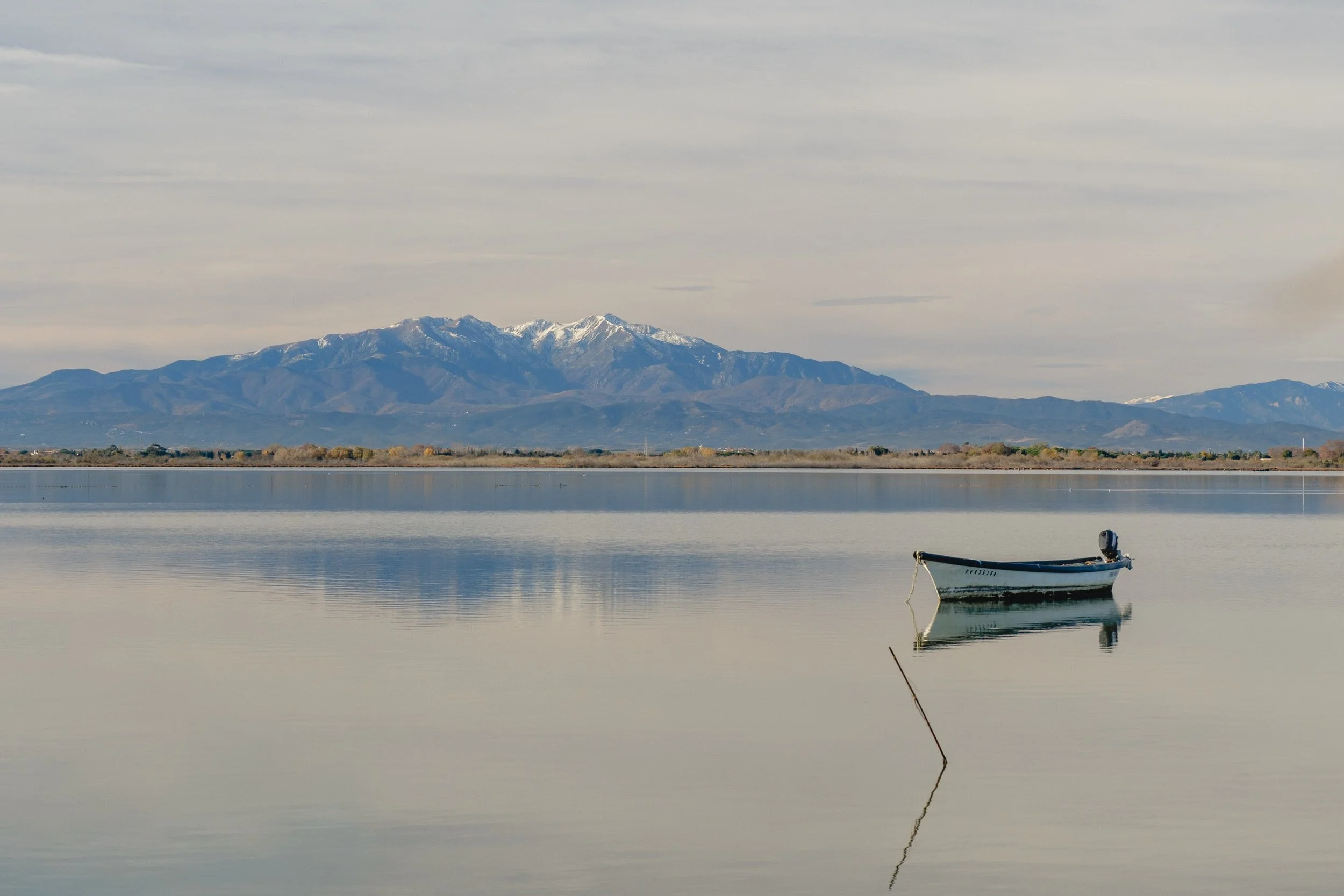 Minimal lake landscape with a solitary boat and distant mountains. A calm fine art photography print.