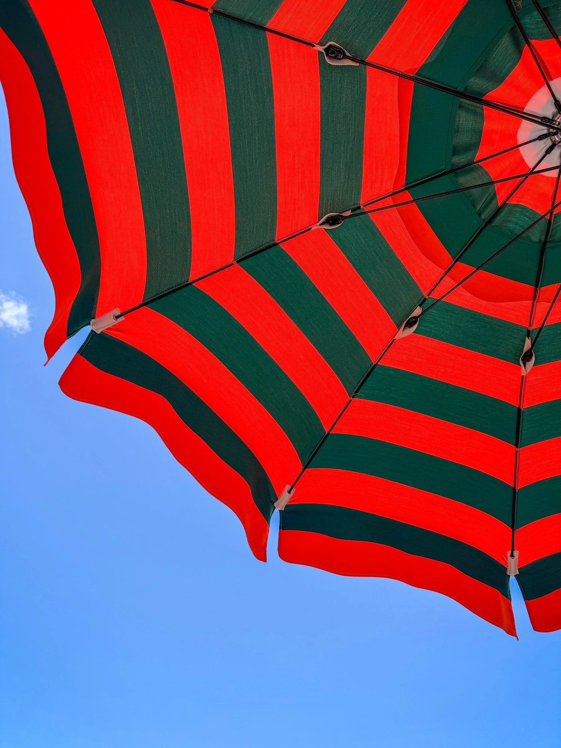 Looking straight up through the ribs of a red and green striped beach umbrella against blue sky