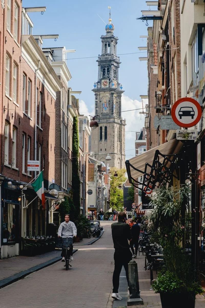 Westerkerk's tower seen down a narrow Amsterdam street as a cyclist passes