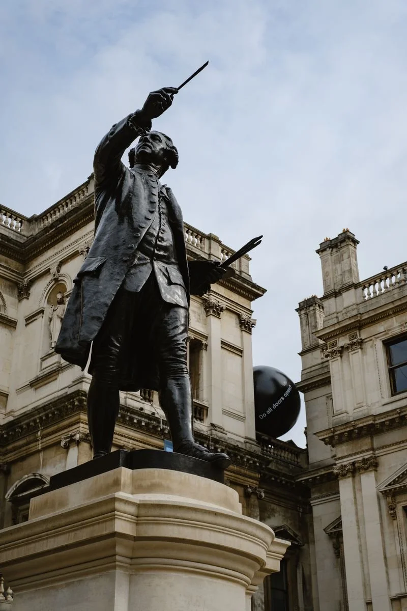 Joshua Reynolds' statue gestures skyward with a paintbrush outside the Royal Academy