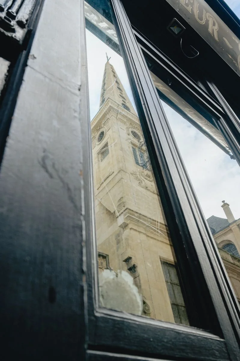 A church spire reflected in the glass of an old shopfront window