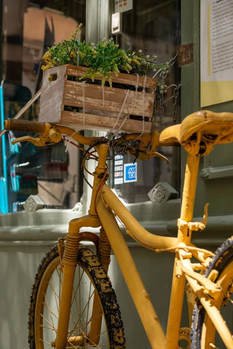 A mustard-yellow vintage bicycle carries a wooden crate of flowers on its handlebars
