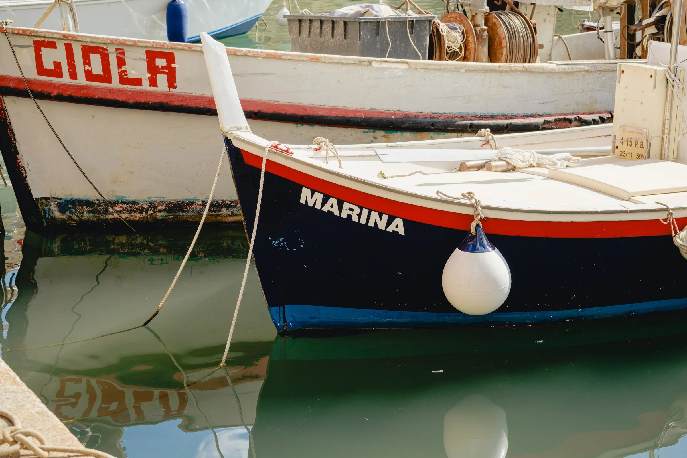 Close-up of two wooden fishing boat bows painted with the names Giola and Marina, hulls touching