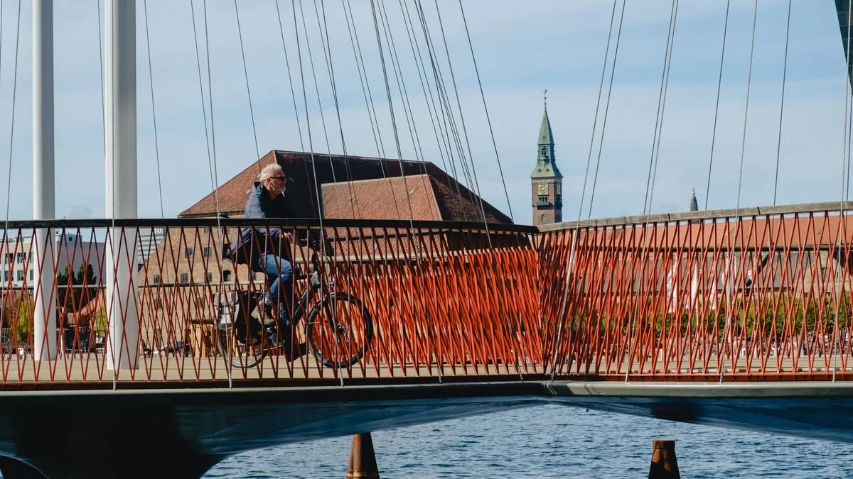 A cyclist crosses a red lattice-cable pedestrian bridge over Copenhagen's harbor
