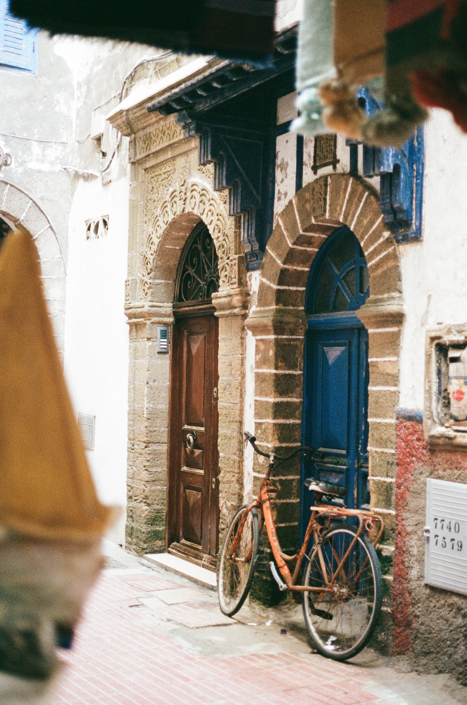 A rusted orange bicycle leans against twin carved stone doorways in Essaouira's medina