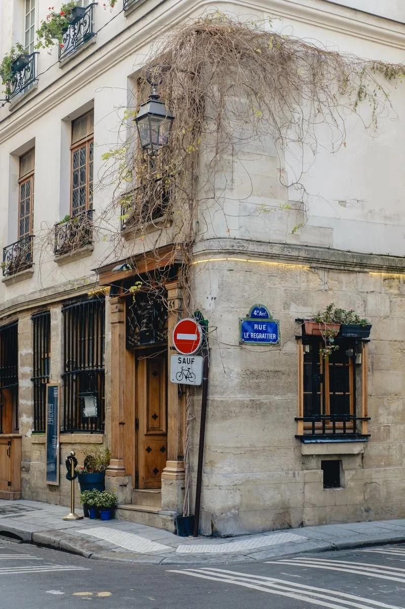 A vine-covered stone corner building at the intersection of Rue Le Regrattier