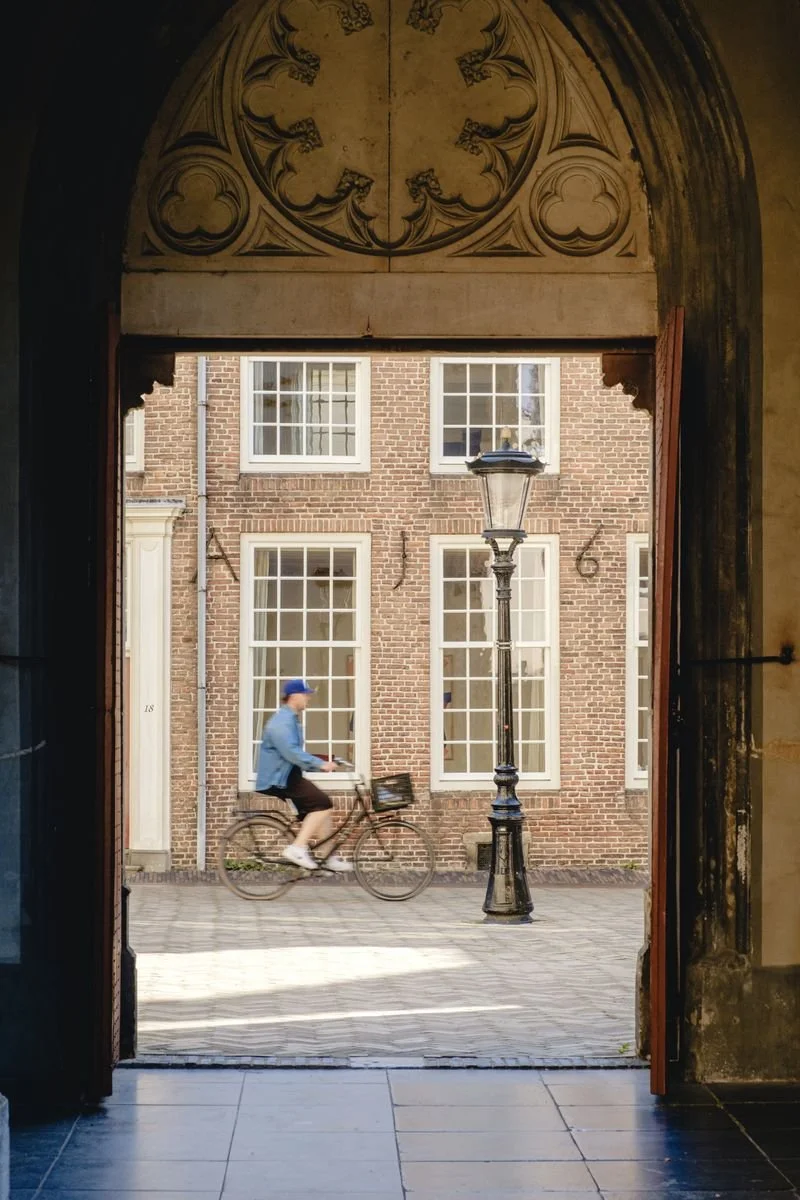 A cyclist passes through a carved stone archway into a quiet courtyard
