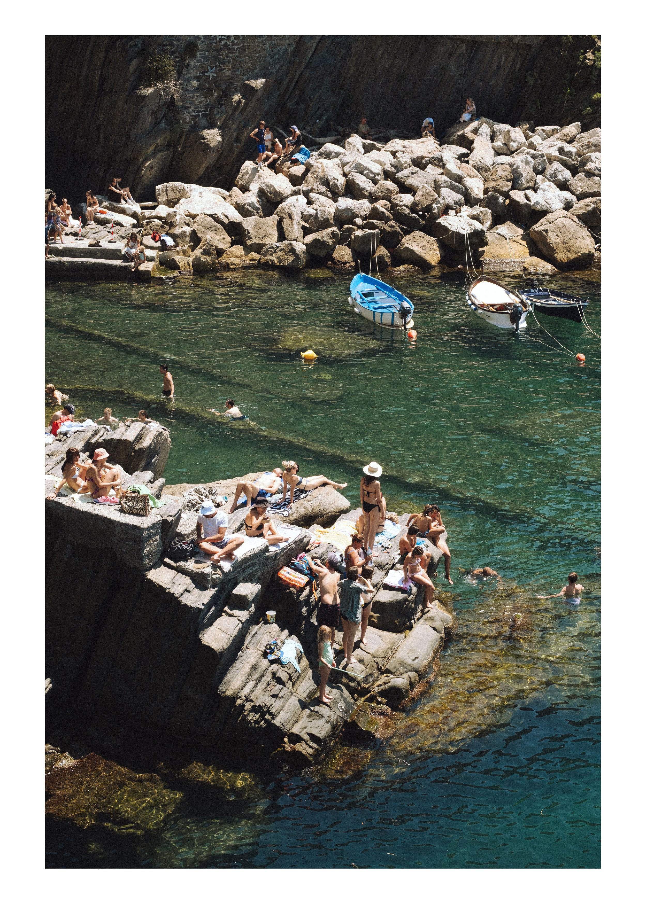 Swimmers and sunbathers on rocks above a turquoise cove, Cinque Terre