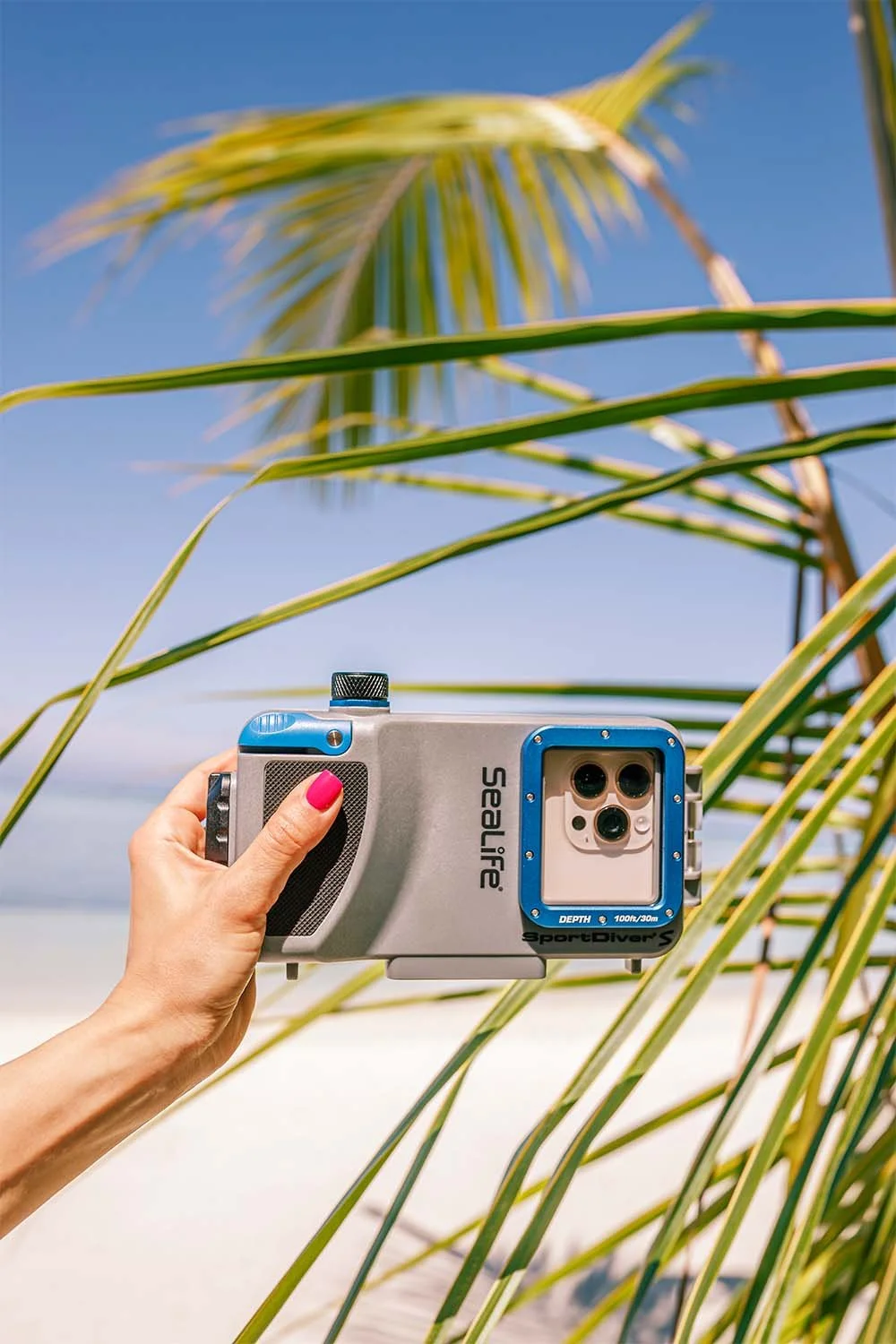 SeaLife SportDiver S phone housing held against a beach and palm trees