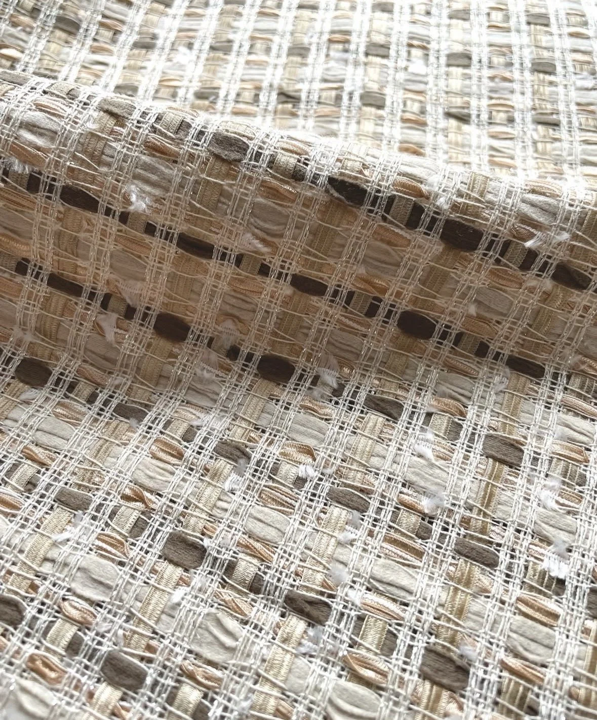 Close-up of a woven, textured fabric with a pattern of intersecting lines and various shades of beige, brown, and cream.