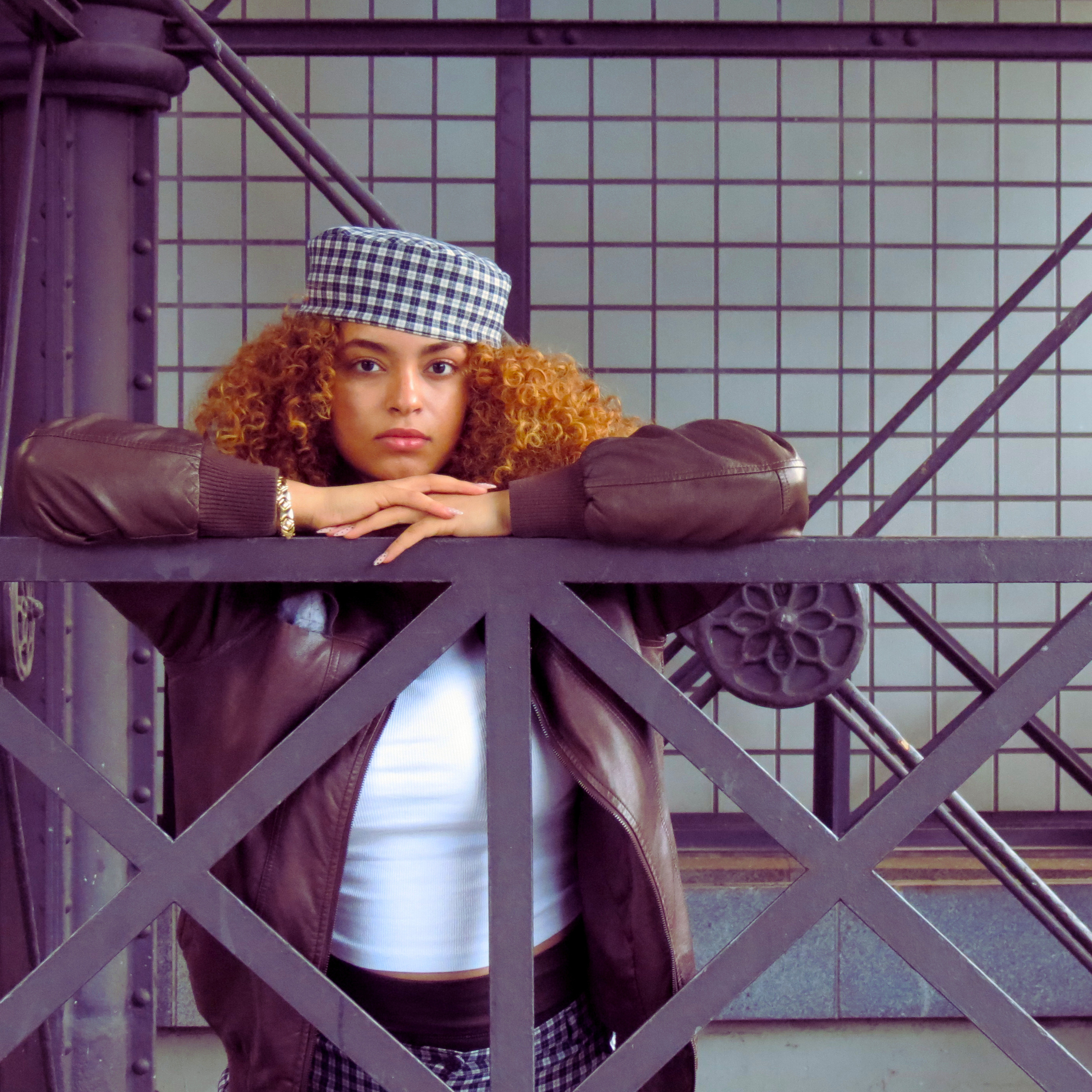 Sarah Edoghogho poses confidently for portfolio picture, wearing a checkered outfit with matching cap, dark jacket, tights, and black boots.