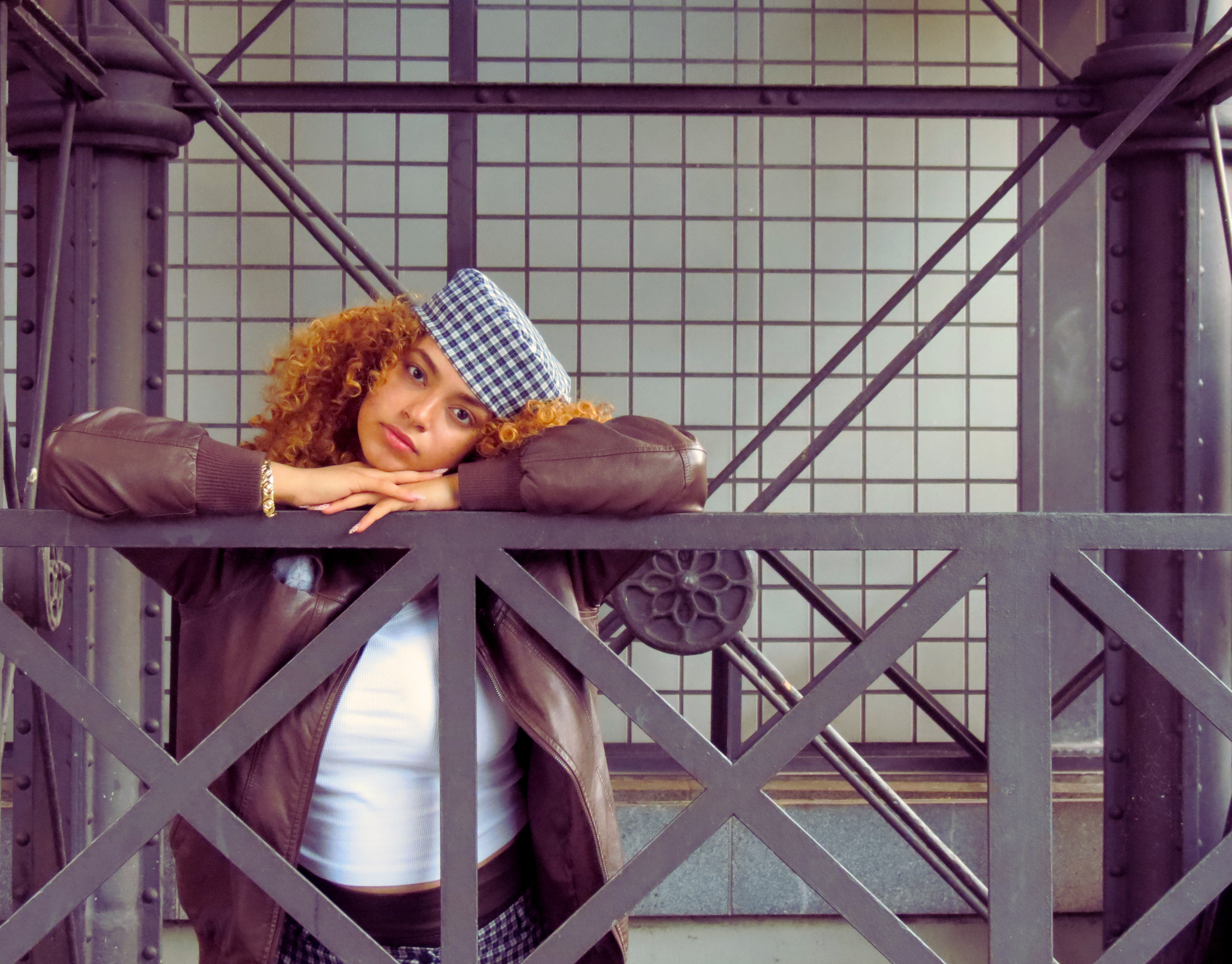 Sarah Edoghogho poses confidently for portfolio picture, wearing a checkered outfit with matching cap, dark jacket, tights, and black boots.