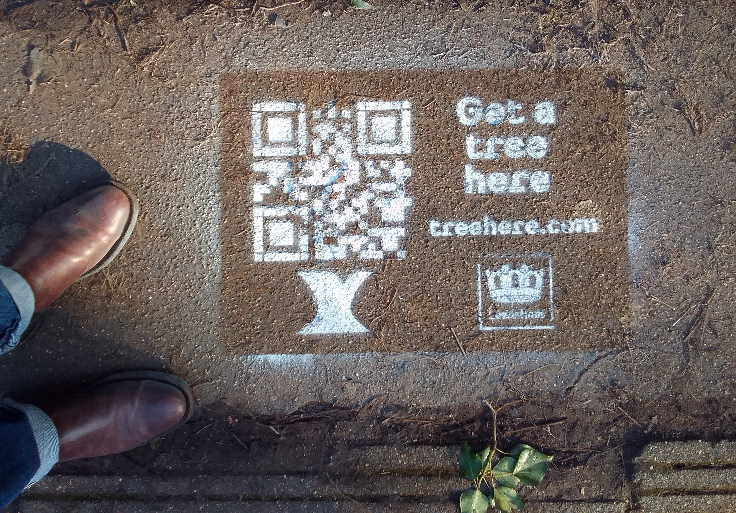 A stenciled advertisement on the ground showing a QR code, text reading 'Get a free check', a website 'techere.com', and a crown symbol, with a person's feet and boots visible in the corner.