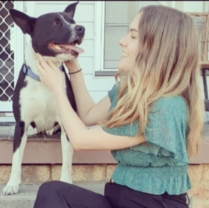 Prue Barrington Naturopath smiling at a black and white dog, holding its face with both hands, on a porch.