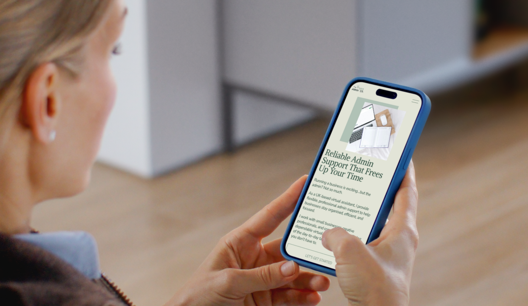 A person holding a smartphone displaying a webpage about admin support services, with a picture of a laptop, notebooks, and a phone.
