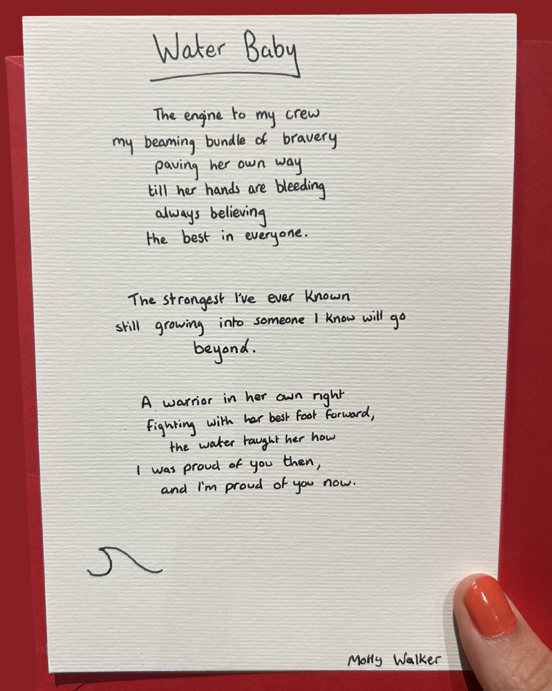 A handwritten poem titled 'Water Baby' on white paper, with a small doodle at the bottom left corner. The poem is signed 'Molly Walker' and the paper is held with a finger with orange nail polish, against a red background.