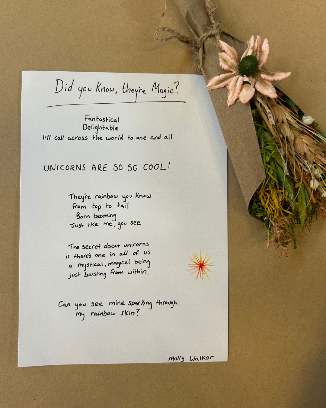 A handwritten note titled 'Did you know, they're Magic?' on a white sheet of paper with a small colorful starburst drawing at the bottom right corner. The note contains a whimsical poem about unicorns. Next to the paper, there is a bouquet of dried f