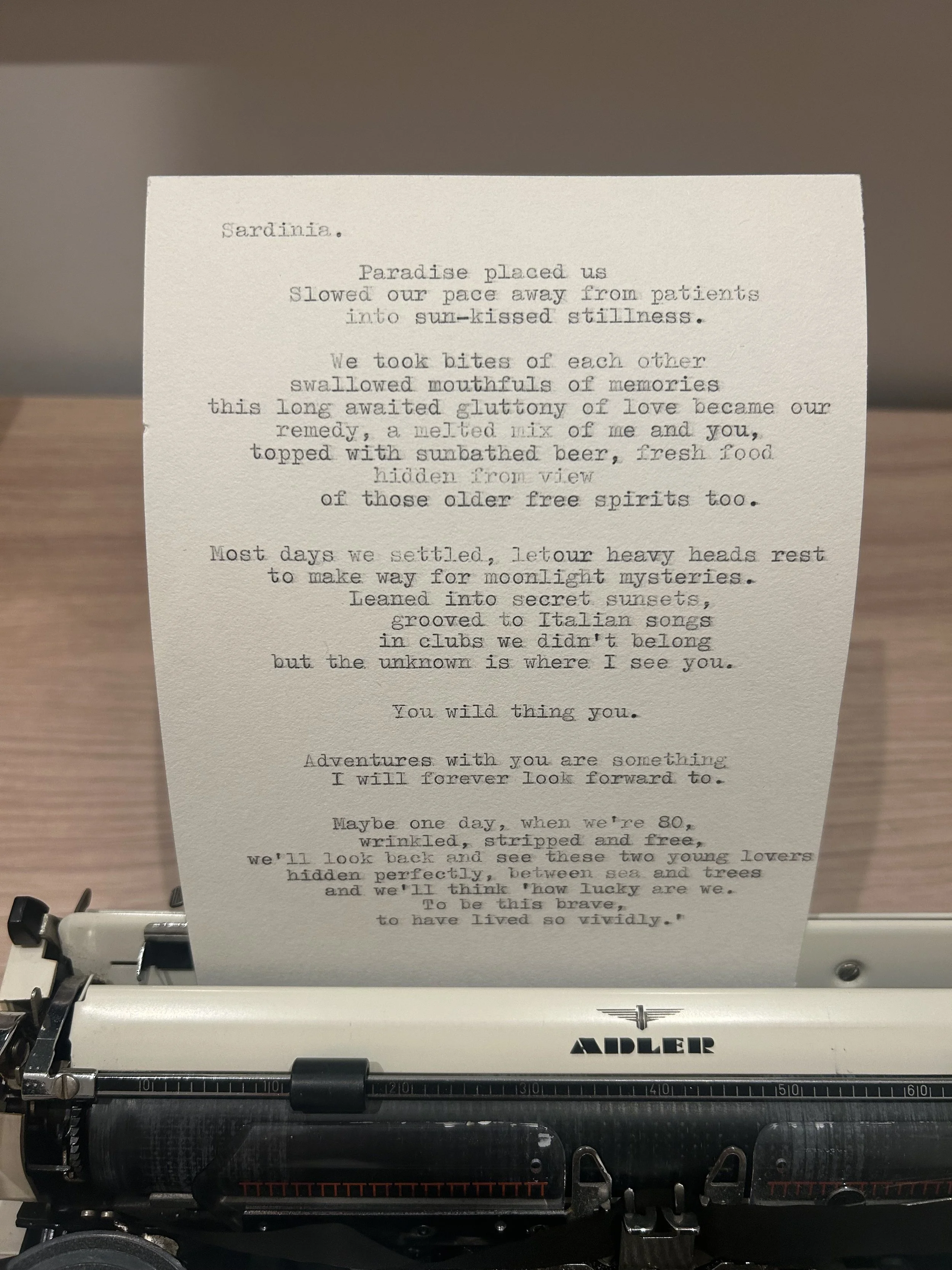 A typewriter printing a poem titled 'Sardinia' on a sheet of paper.