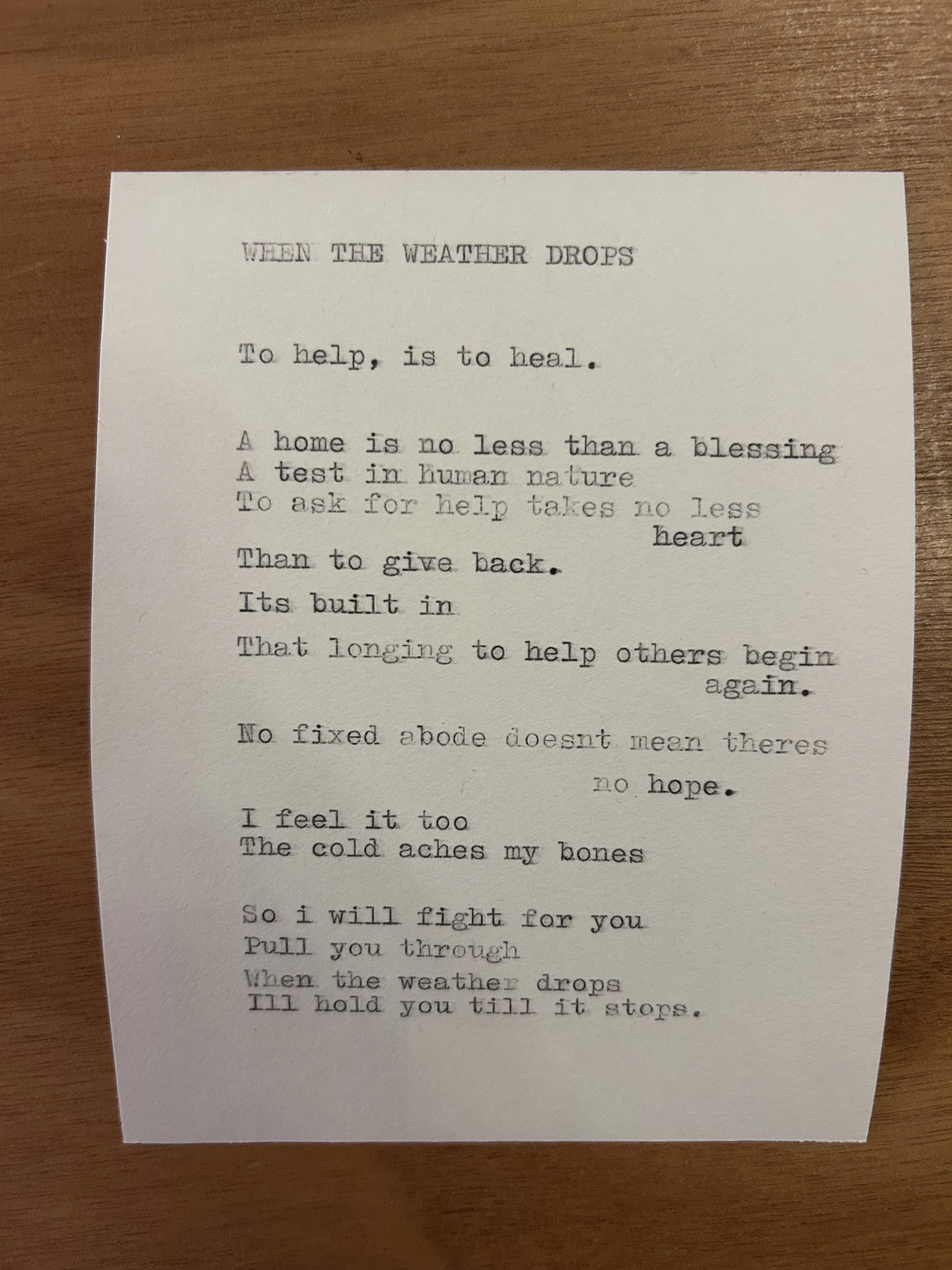 A printed poem titled 'When the Weather Drops' on a sheet of paper placed on a wooden surface.