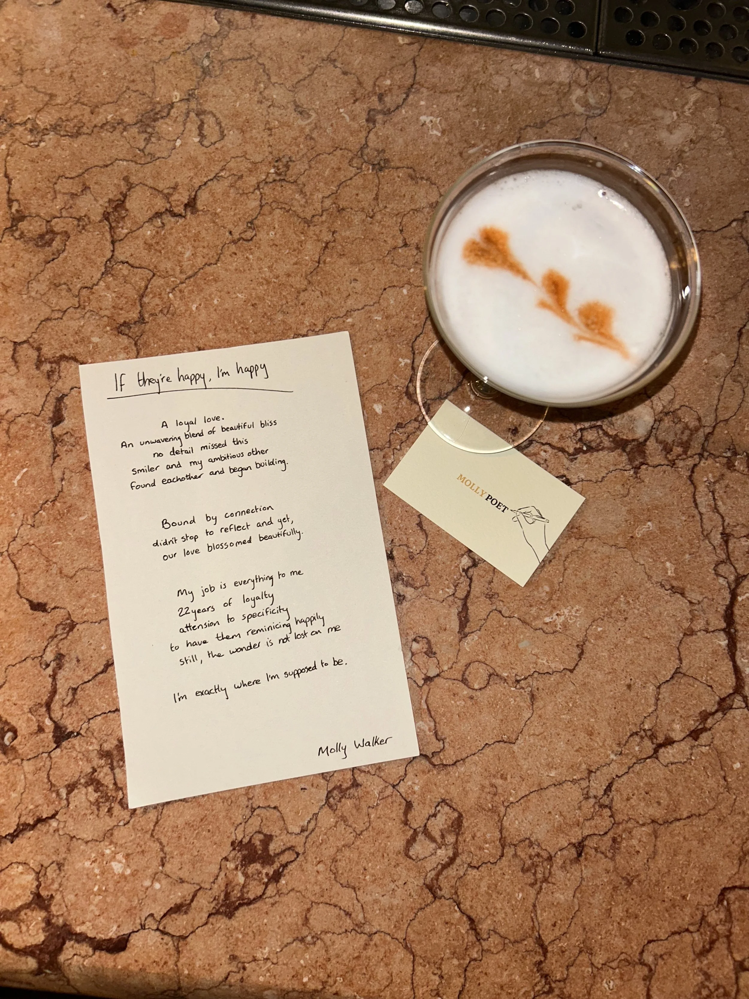 A handwritten poem titled 'If they're happy, I'm happy' alongside a cup of latte on a marble countertop. The poem is signed by Molly Walker, and there is a business card with her name and a pencil sketch of a hand holding a pen.