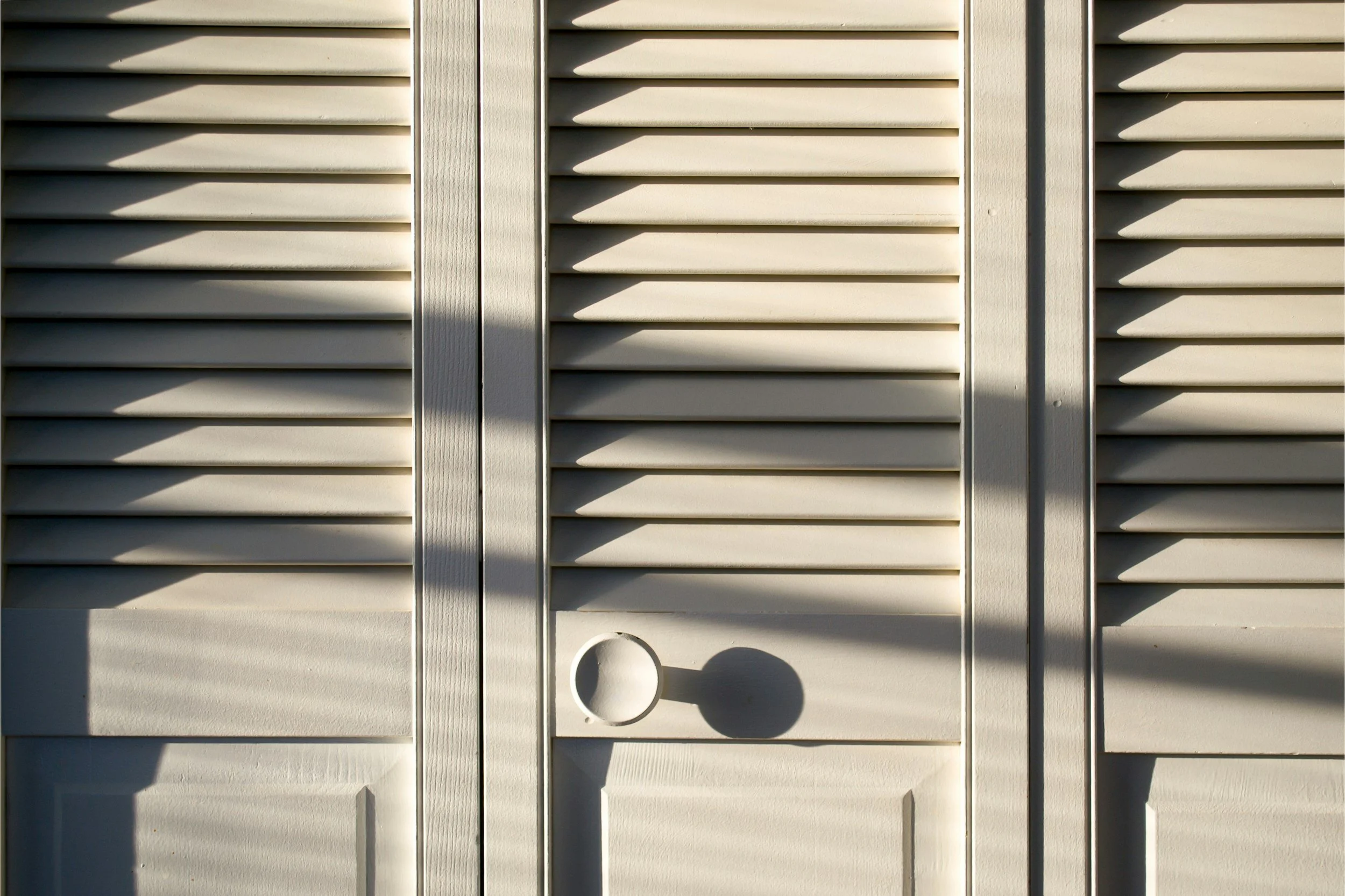 Close-up of beige window shutters with shadows cast by sunlight.