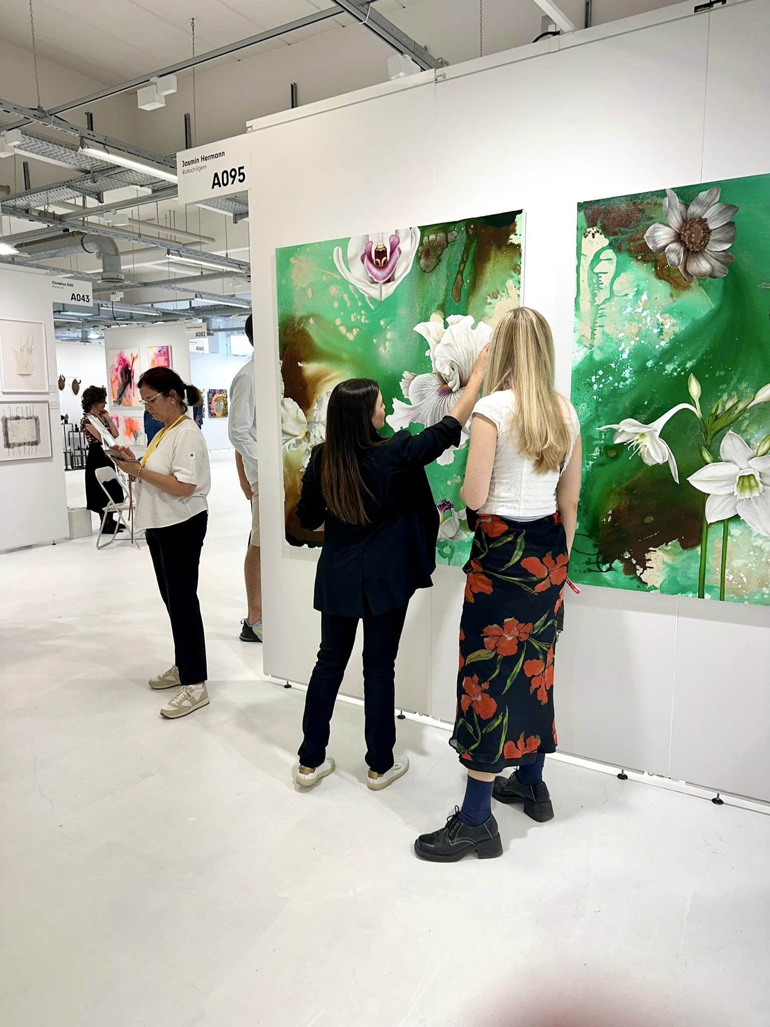 People viewing and discussing floral artwork at an art exhibition.