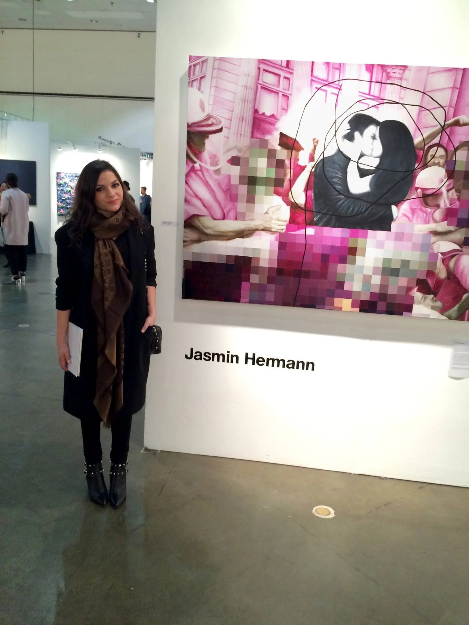 A woman standing next to an art display at a gallery. The artwork features a couple in an embrace, with pixelated and graphic elements, and is signed by Jasmin Hermann.