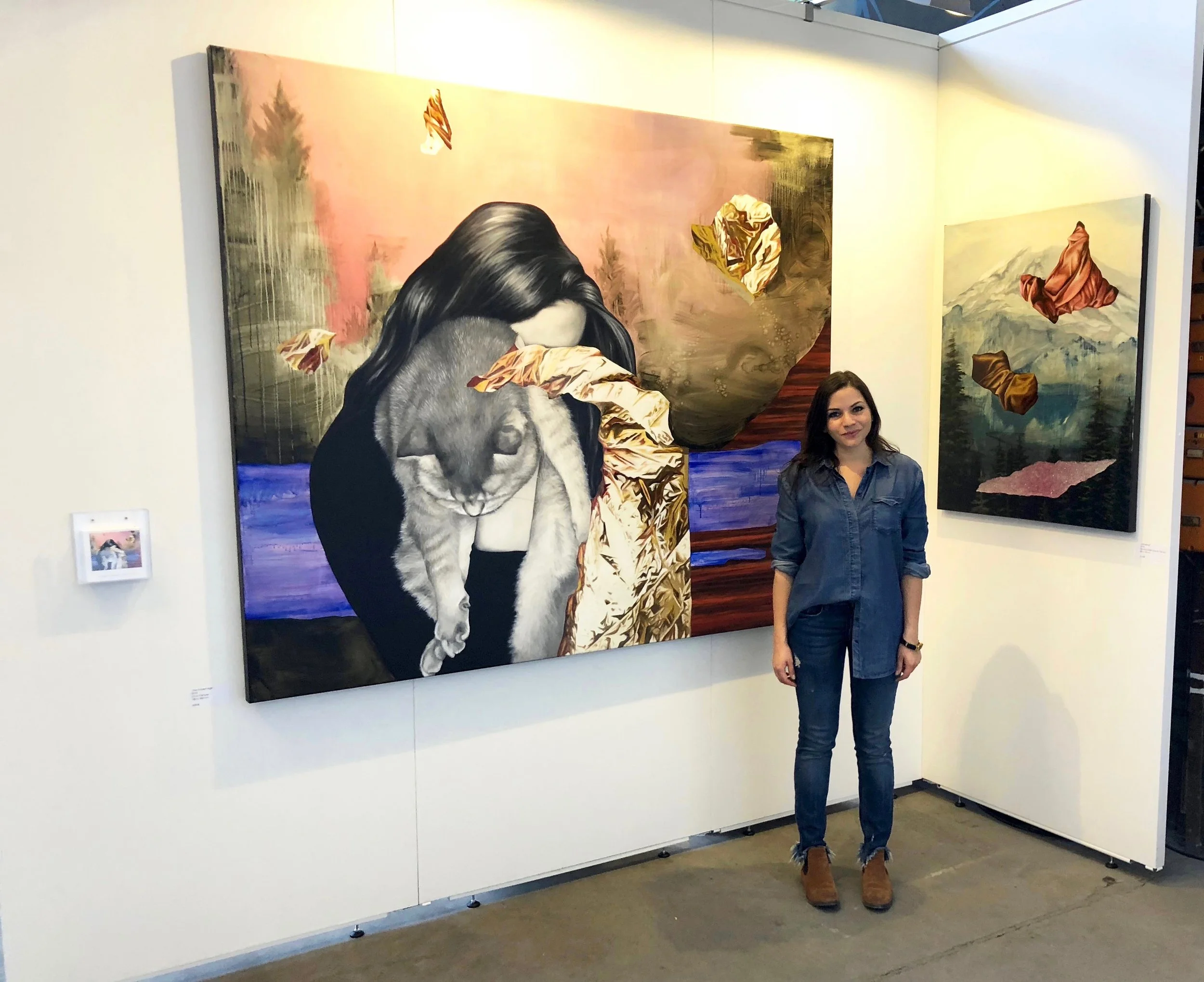 A woman standing in an art gallery next to a large portrait of a girl holding a cat, with painted leaves and landscape backgrounds.