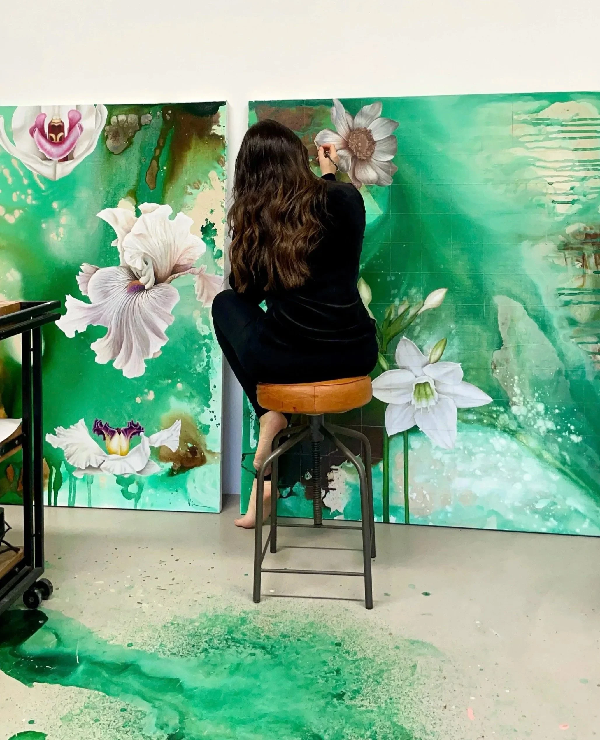 An artist painting large, detailed floral murals with white and purple flowers on a green abstract background.