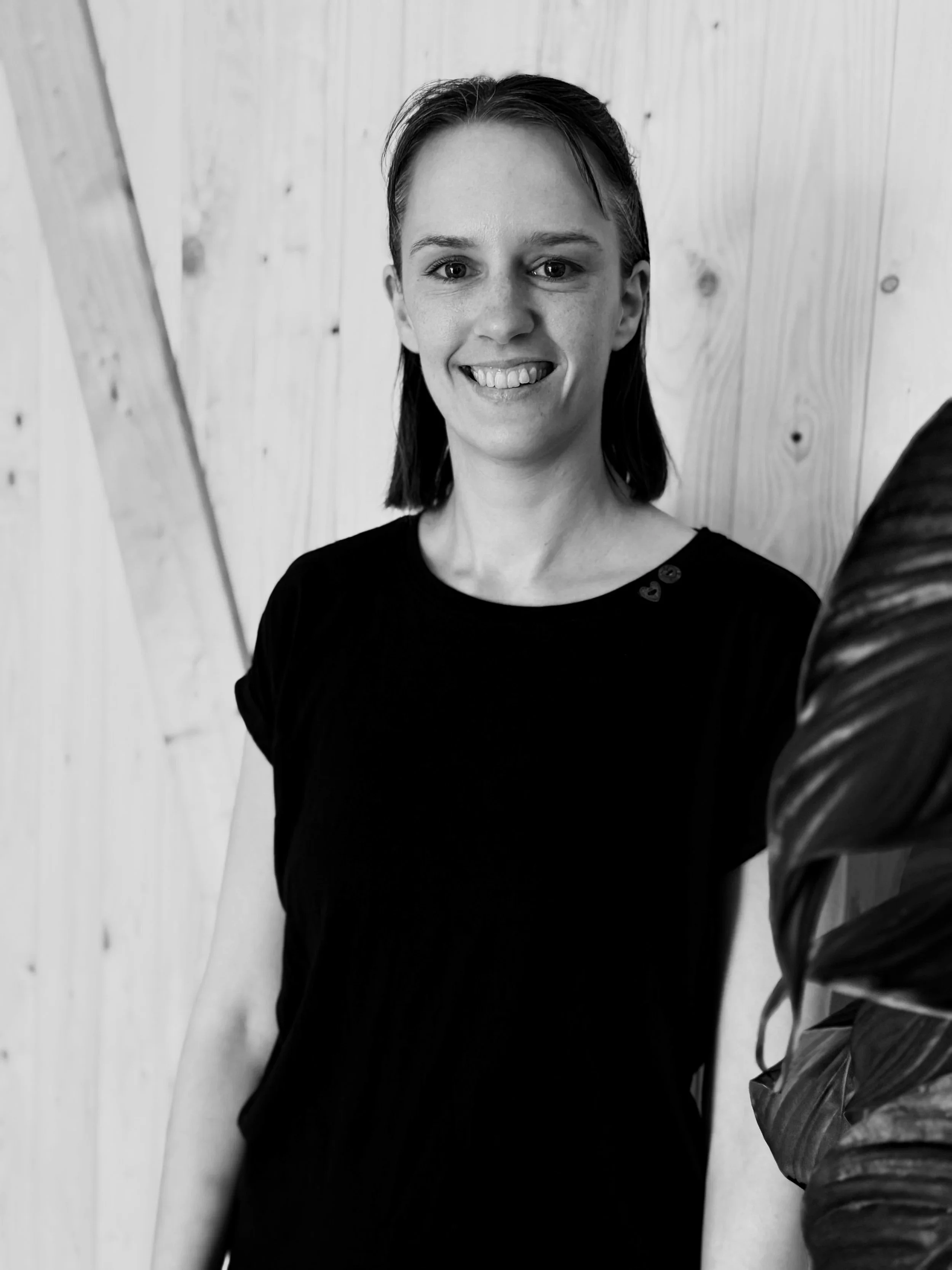 Schwarz-Weiß-Foto einer lächelnden Frau, die vor einer Holzwand steht.