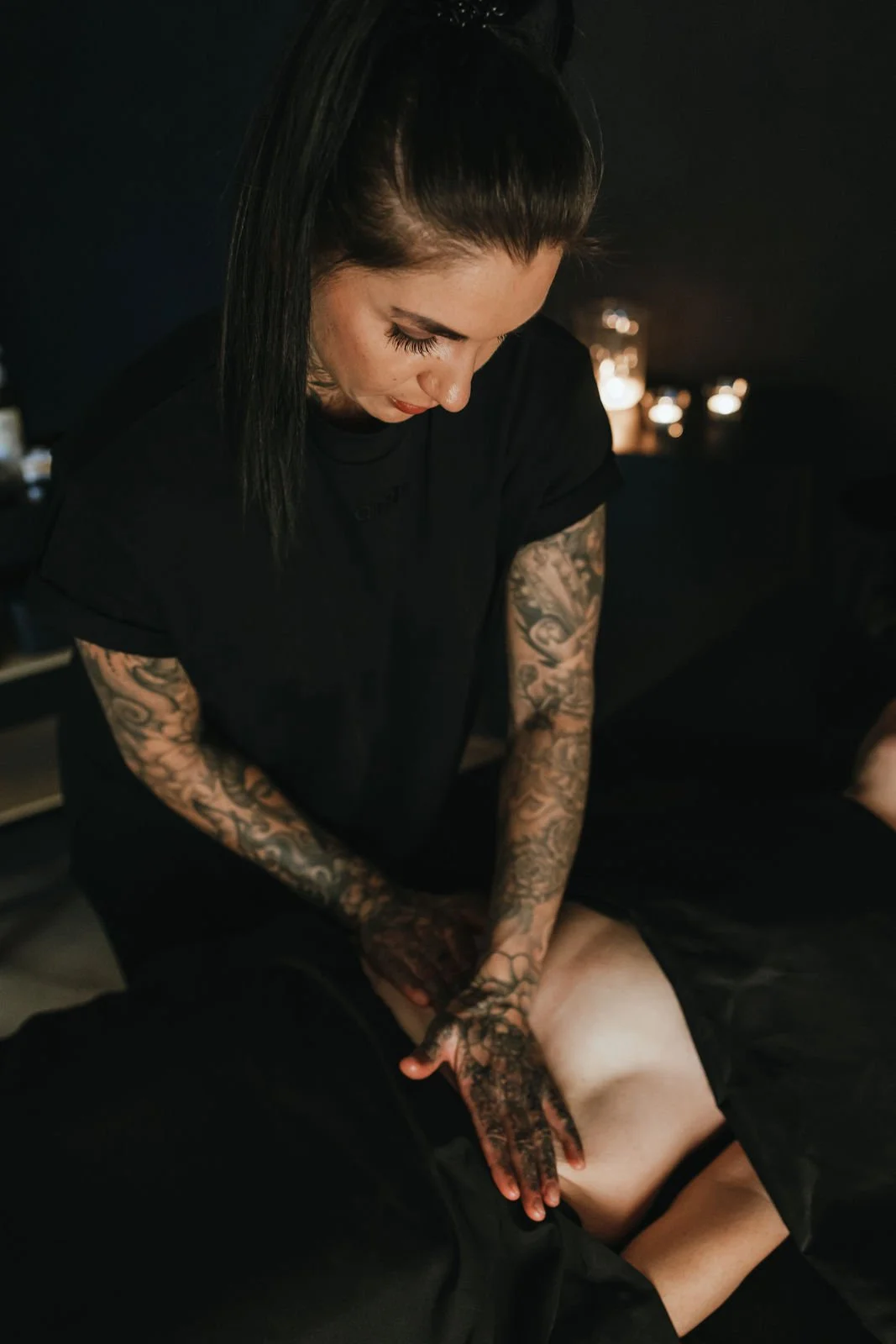 Tattooed masseuse arbeitet an einem Rücken in einem dunklen Raum.