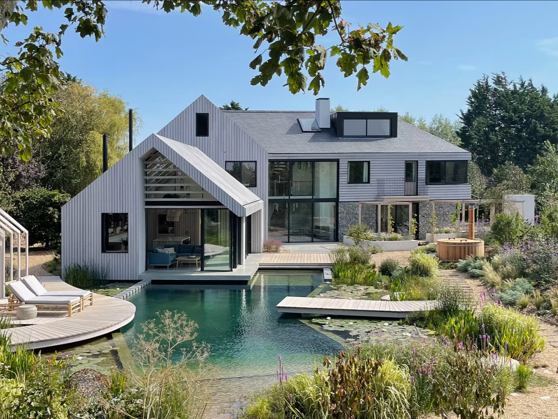 Modern house with large glass doors, a swimming pool, and surrounding greenery on a sunny day.