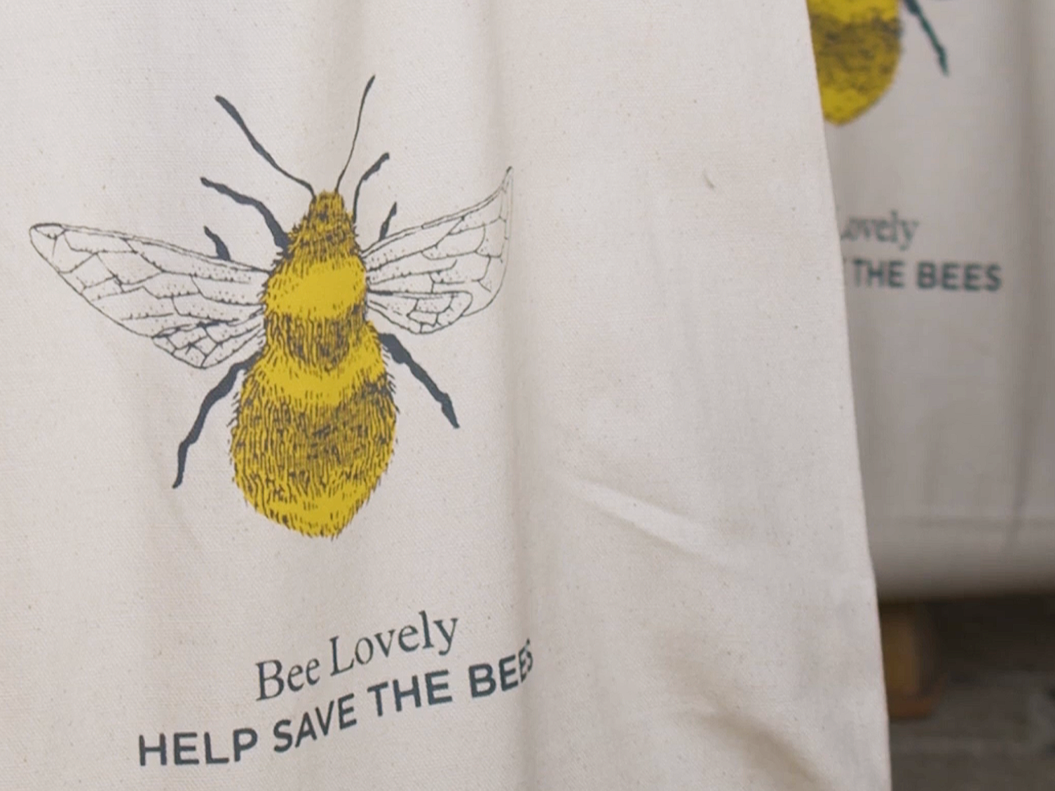 A fabric bag featuring a yellow and black illustration of a bee with the words "Bee Lovely HELP SAVE THE BEES" printed on it.