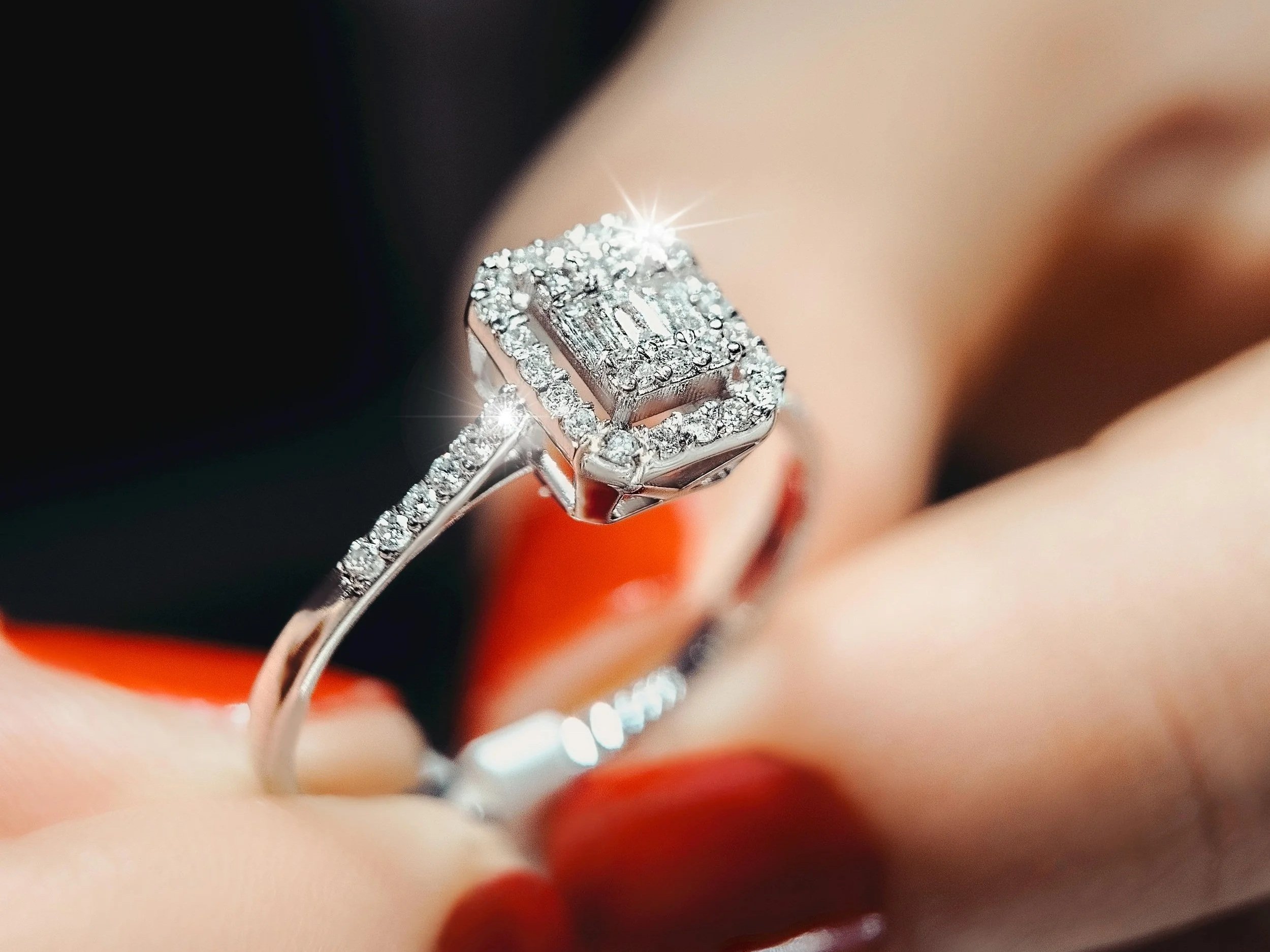 Close-up of a diamond ring with multiple small diamonds and a large central diamond, held between fingers.