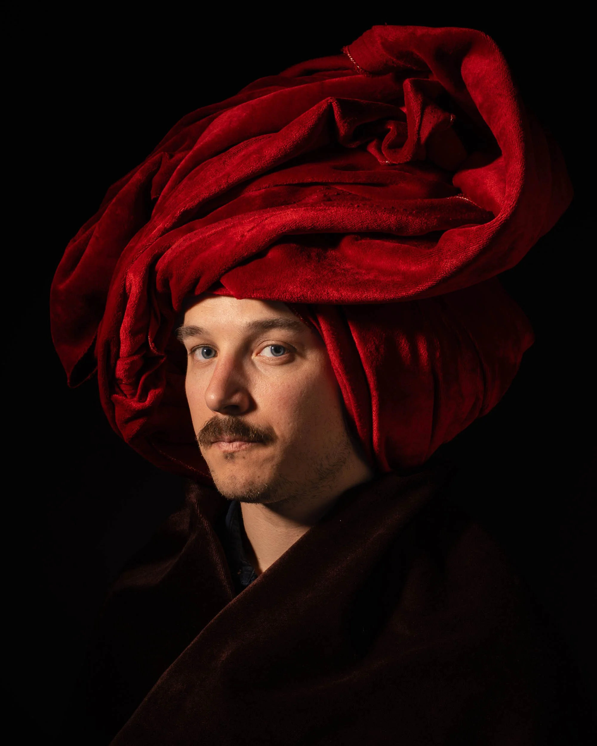 Portrait d’un homme portant un large turban rouge sur fond noir.
