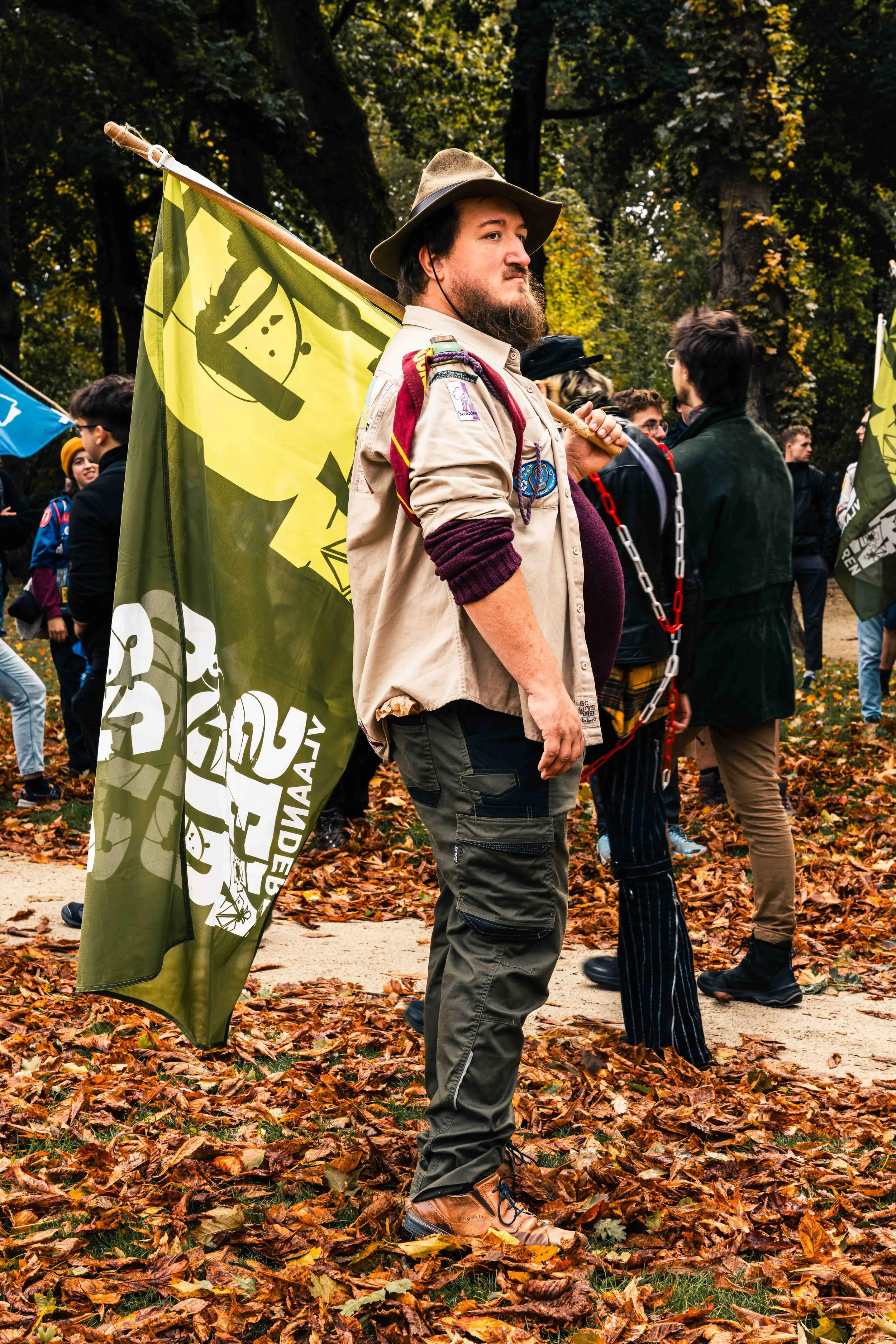 Photographie de reportage réalisée lors d’une mobilisation citoyenne dans un parc urbain. Un participant portant un drapeau se tient au premier plan, entouré d’autres manifestants rassemblés dans un paysage d’automne. L’image capture l’atmosphère du 