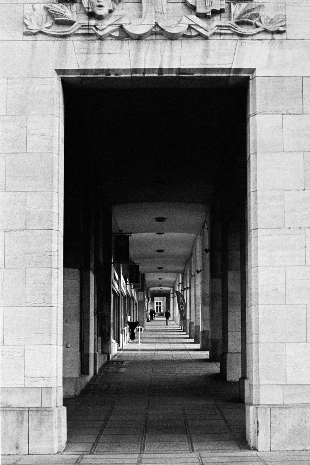 Photographie d'architecture en noir et blanc montrant une galerie couverte avec une perspective marquée et des passants, réalisée à Bruxelles.