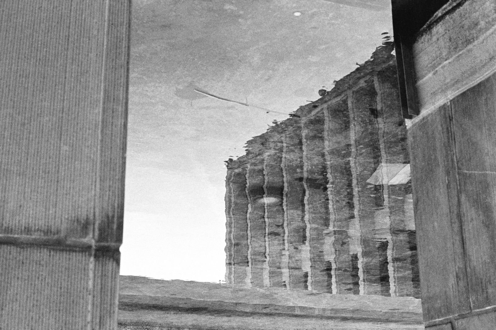 Photographie d'architecture en noir et blanc représentant le reflet déformé d'un bâtiment moderne dans l'eau, réalisée à Bruxelles.