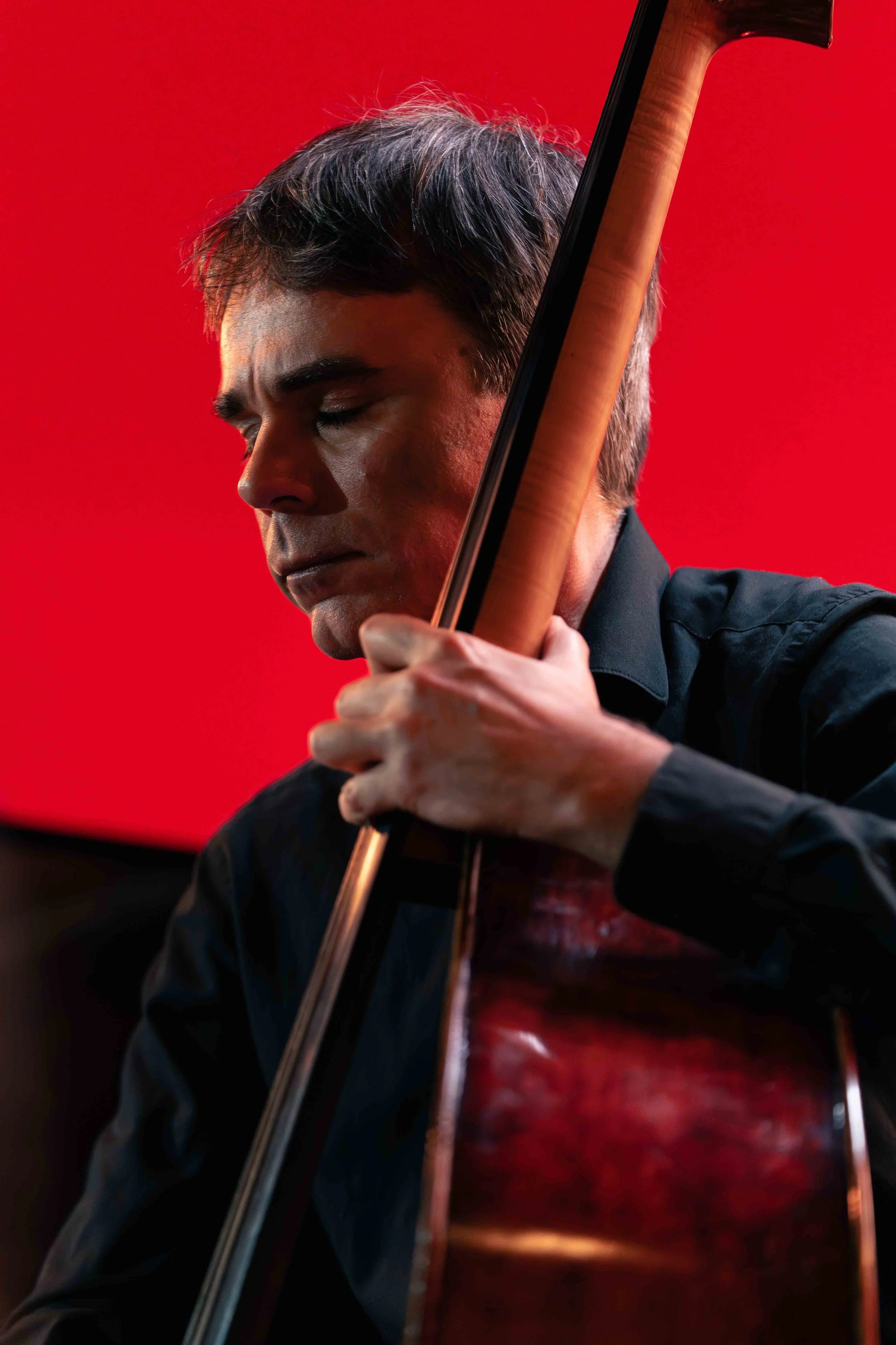 Portrait d’un musicien sur fond rouge. Lumière latérale mettant en valeur l’instrument et la concentration du sujet.