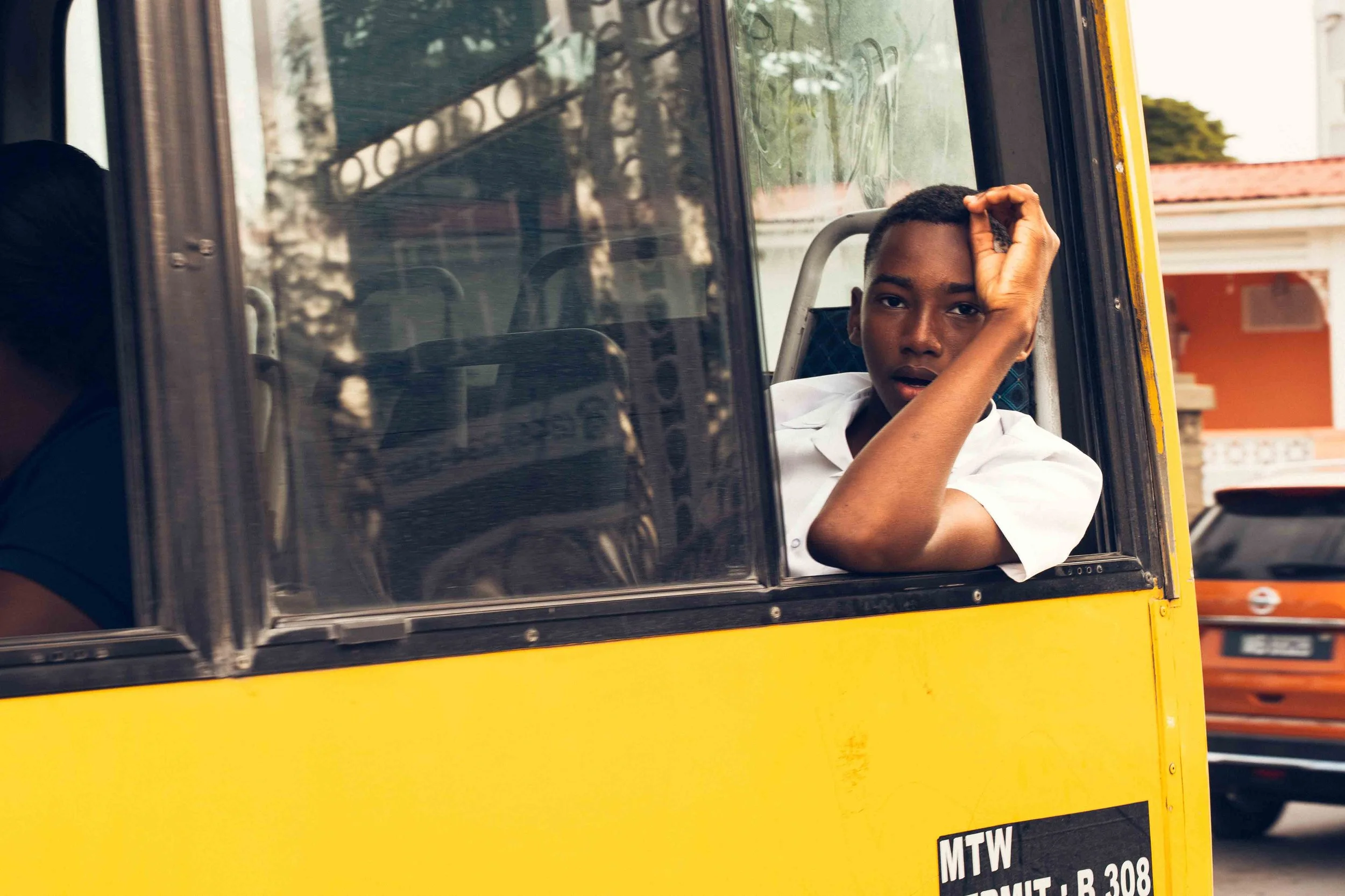 Photographie documentaire montrant un élève regardant par la fenêtre d’un bus scolaire jaune. Le portrait pris sur le vif capte un moment de pause pendant un trajet quotidien, avec le regard dirigé vers l’extérieur et la lumière naturelle entrant dan
